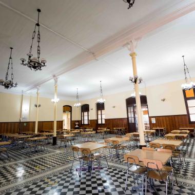 Interior del Casino Central de comida de la Universidad visto desde una esquina. En la foto se pueden apreciar numerosas mesas y sillas. En el techo se ubican lámparas colgantes blancas.