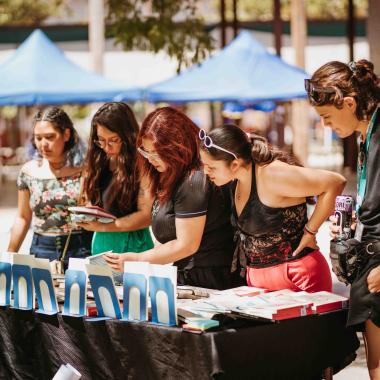 Cinco jóvenes revisando libros de un stand en una feria al interior de la Escuela de Artes y Oficios (EAO).