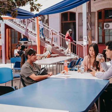 Tres estudiantes comiendo sentadas y sentados en una de las mesas fuera del casino central. 