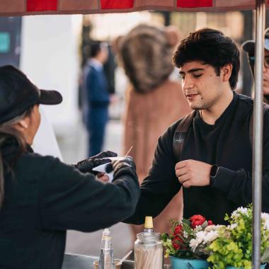 Un joven está recibiendo un café en un vaso de una mujer que está atendiendo en un carrito que ofrece estos bebestibles durante la mañana al interior del campus.