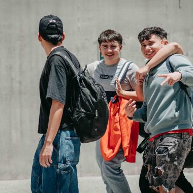 Cuatro amigos riéndose abrazados y caminando por el campus. 