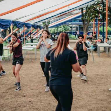 Plano general de seis jóvenes practicando defensa personal de frente a una profesora guía que está de espaldas a la cámara.