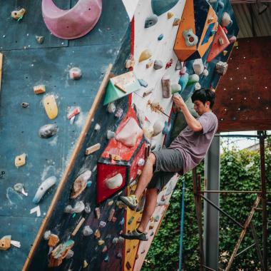 Plano entero de un joven escalando un muro. Su cuerpo está de perfil y el muro que sube está inclinado.