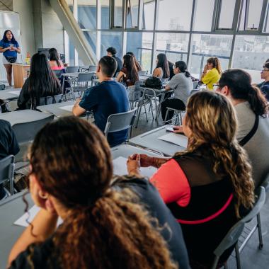 Alumnos sentados en una sala de clases, viendo una presentación. 