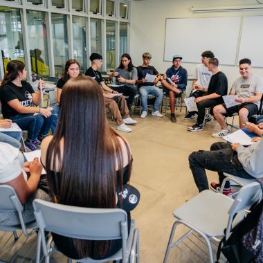 Alumnado sentado en un circulo mientras realizan una actividad