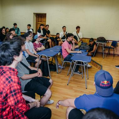 Alumnos sentados en una sala de clases, escuchando una presentación. 