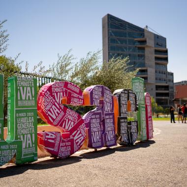 Se ven las letras que se encuentran en el frontis "usach" decoradas con afiches sobre la huelga del ocho de marzo