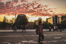 Foto ganadora concurso. Estudiante camina por fuera de entrada principal usach y frente al planetario en una tarde en cae el sol.