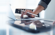  Hand of a person holding a pencil, while checking their computer.