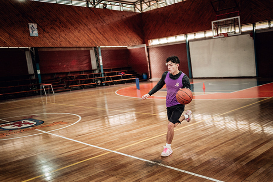 Jugador de básquetbol boteando balón en gimnasio  