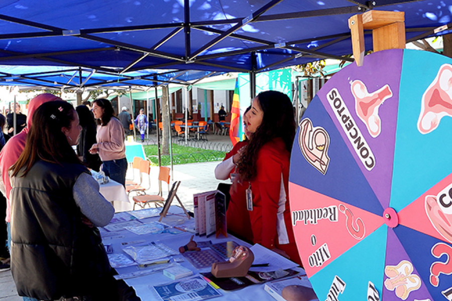 Asistentes a la feria reciben información bajo toldo azul