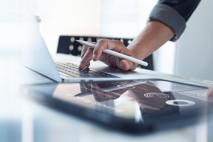  Hand of a person holding a pencil, while checking their computer.