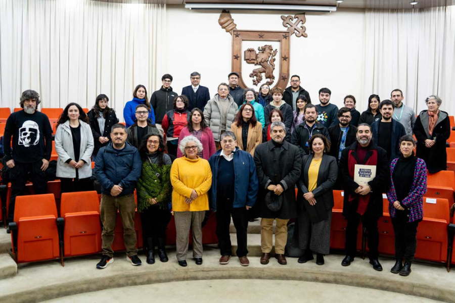 Decano de la Facultad de Ciencias Médica posa en cámara junto a los asistentes a la seminario. Se encuentran en el Salón de Honor y en el fondo se presencia el emblema de la Universidad hecho en madera.