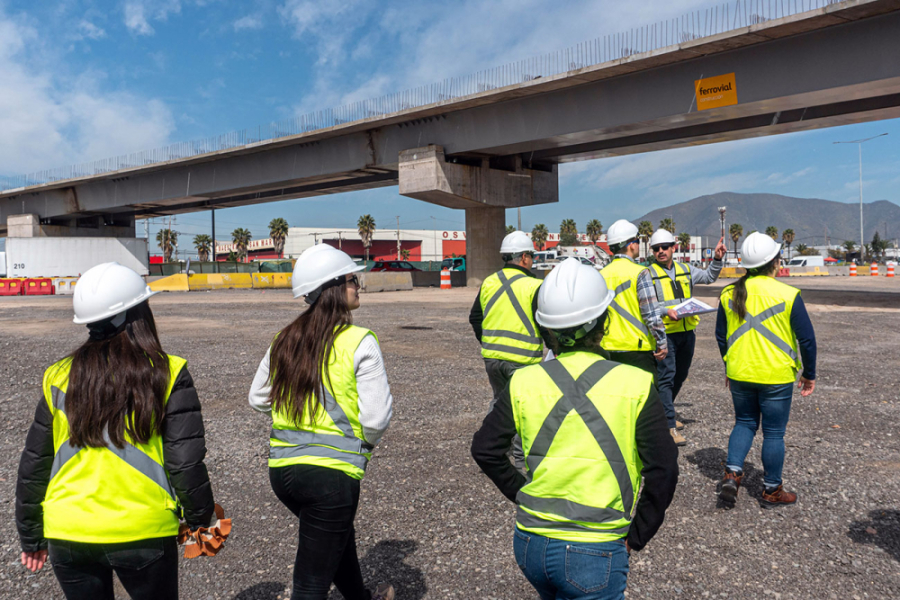 Ingenieros caminan bajo un trébol vial. Portan cascos blancos y chalecos amarillos de seguridad