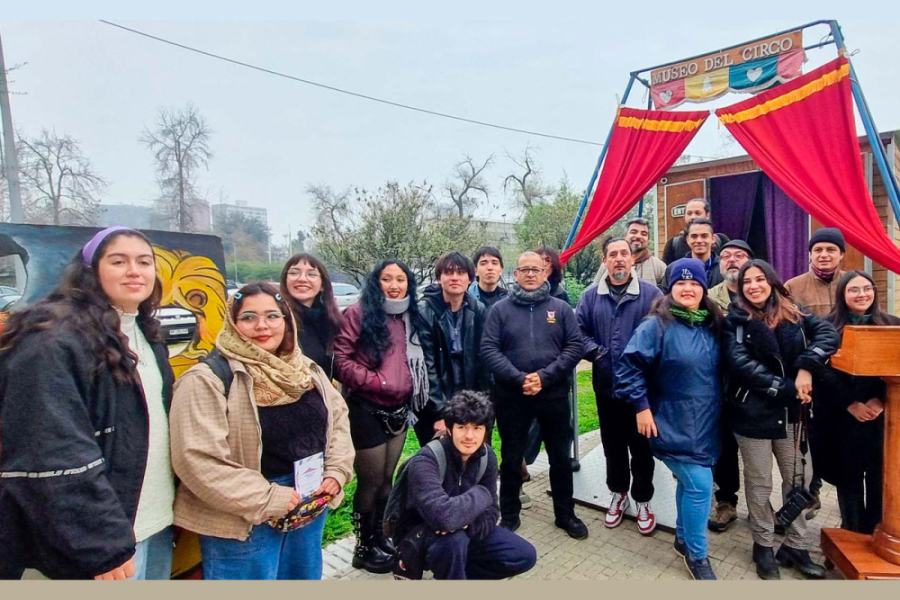 En la fotografía aparecen un grupo de asistentes al Museo Itinerante del Circo, que posan en su fachada en los Patios de Ciencia de la Usach. De fondo, se ve una carpa roja y los trailers que sirven de sala de exposición.