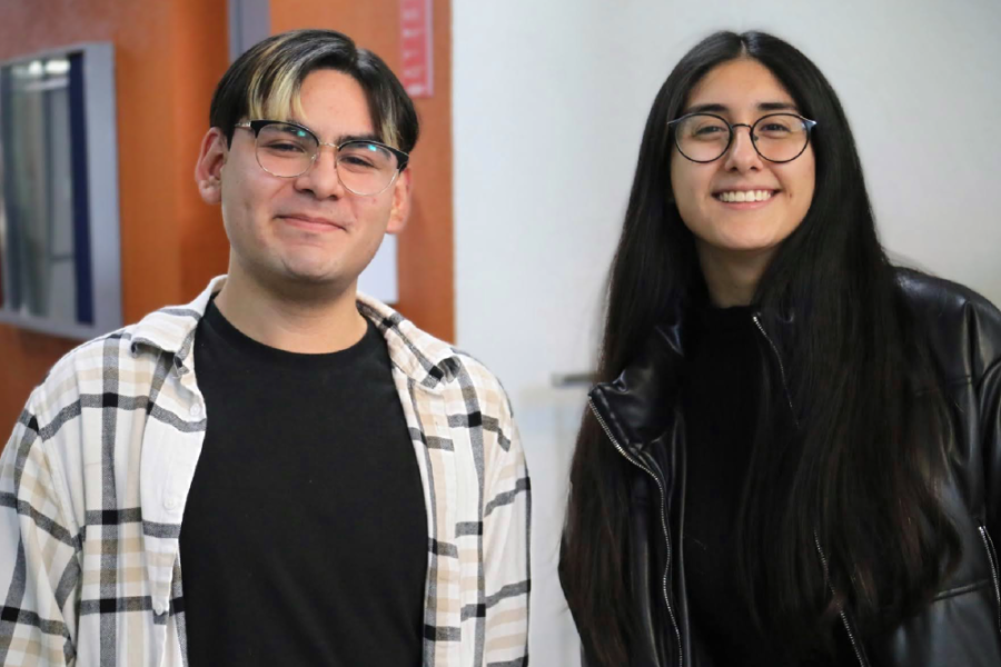 Estudiantes de la Facultad de Química y Biología posan a la cámara. El hombre, lleva una camisa de franela a cuadros grandes de fondo blanco y líneas negra. Le estudiante viste chaqueta y cheleco negro.