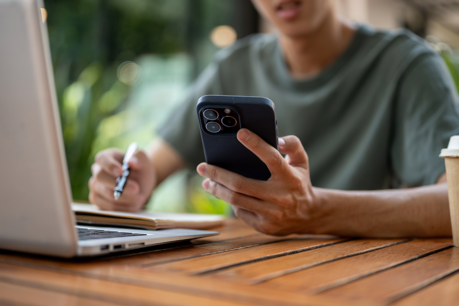 Persona con teléfono celular en la mano, trabajando con un computador.