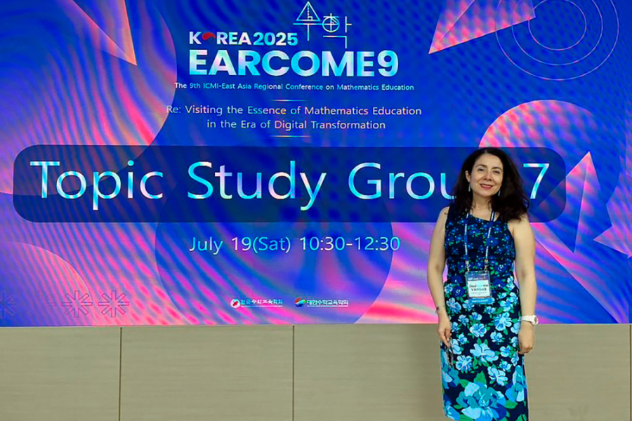 En la fotografía aparece la Dra. Vargas, con un vestido con motivos florales que va de tonalidades negras a celeste del talle al cinto. De fondo, una pantalla con una lámina informativa del congreso en Seúl. Correa del Sur. 