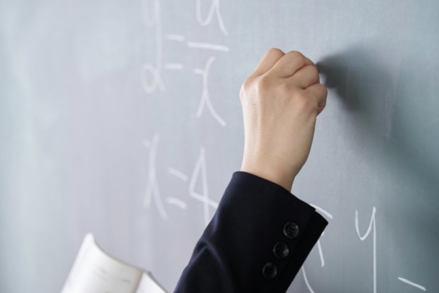 En la fotografía aparece la mano de un profesor escribiendo sobre el pizarrón.