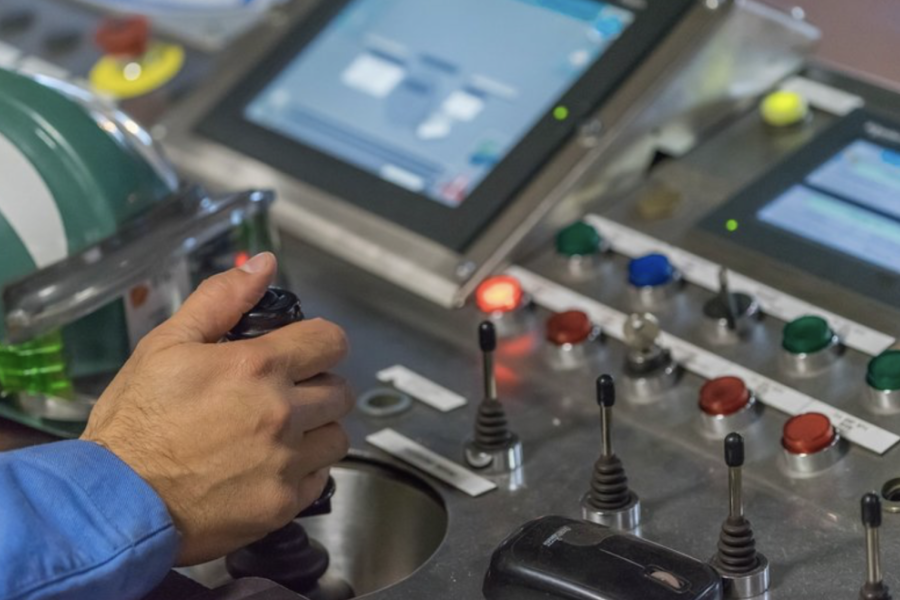 En la fotografía aparece una mano operando una máquina con muchas perillas de control