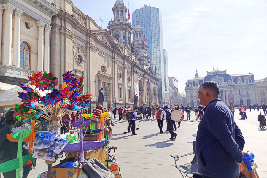 Foto ganadora del concurso Integrarte. La imagen hace una descripción del a Plaza de Armas de Santiago, con un organillero, chinchineros, la gente alrededor y de fondo la Catedral de Santiago y los edificios de Correos de Chile y uno de espejos.