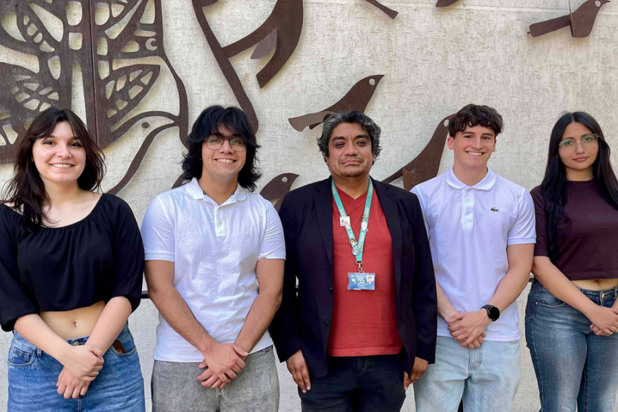 En la imagen aparece un académico y cuatros estudiantes (dos hombres y dos mujeres). De fondo, una escultura realizada por el Premio Nacional de Artes Plásticas, Alejandro "Mono" González, que engalana la fachada del edificio de Bachillerato Usach