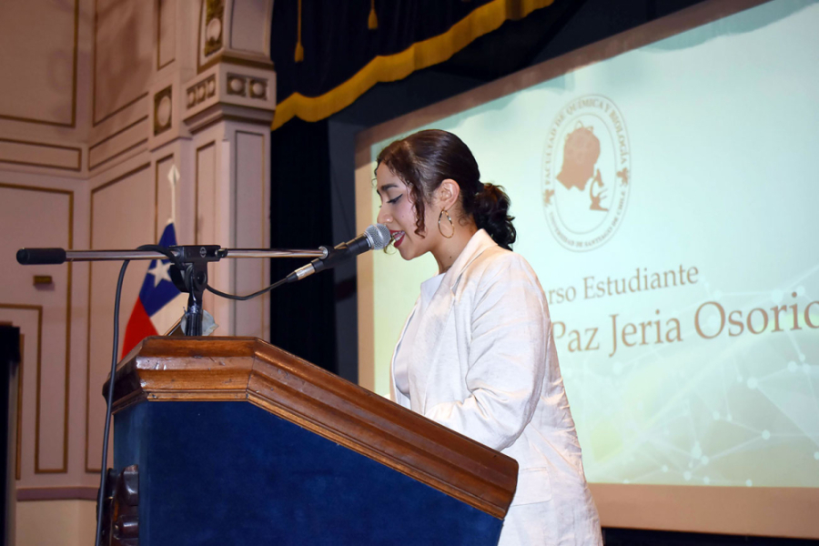 En la fotografía aparece una estudiante de la Facultad, realizando un discurso desde el podio del Teatro Aula Magna Usach