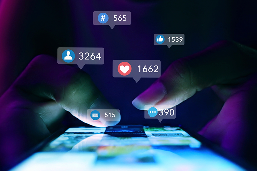 Close-up of hands using a smartphone in the dark, with glowing 3D notification icons for likes, hearts, and messages floating above.