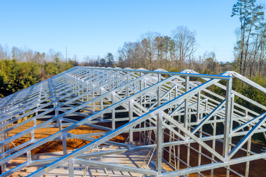 Close-up of a large, silver metal roof frame under construction against a clear blue sky.