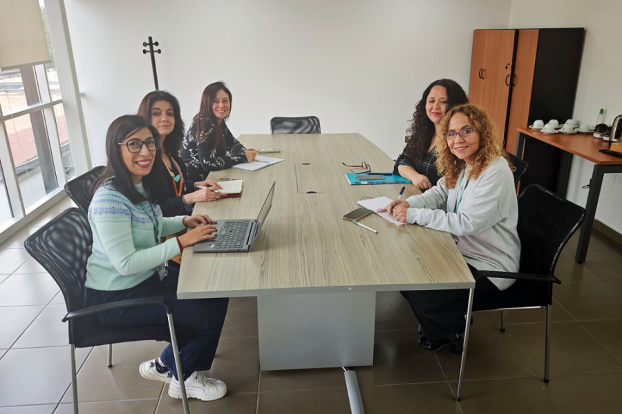 En la imagen, las cinco mujeres que de la Vipo, que se encuentran trabajando en el programa. Sentadas y reunidas con insumos sobre una mesa, mirando hacia la cámara 