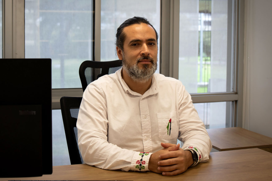 En la imagen aparece el Dr. José Ponce, investigador del Departamento de Historia en su oficina. Sentado y con las manos cruzadas sobre una mesa.
