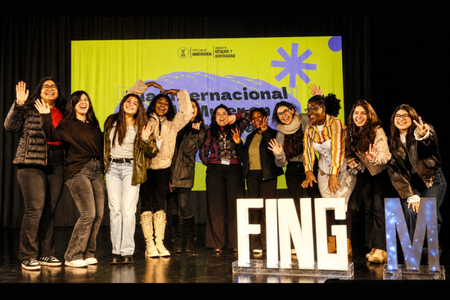 En la imagen aparecen una docena de estudiantes que posan a la cámara en el escenario central de la actividad con unas letras grandes que indican FING M que se refiere a Facultad de Ingeniería Mujeres