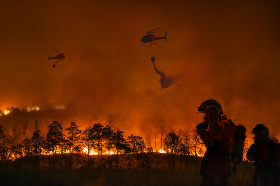 Bomberos combaten un enorme incendio forestal mientras helicópteros lanzan agua.