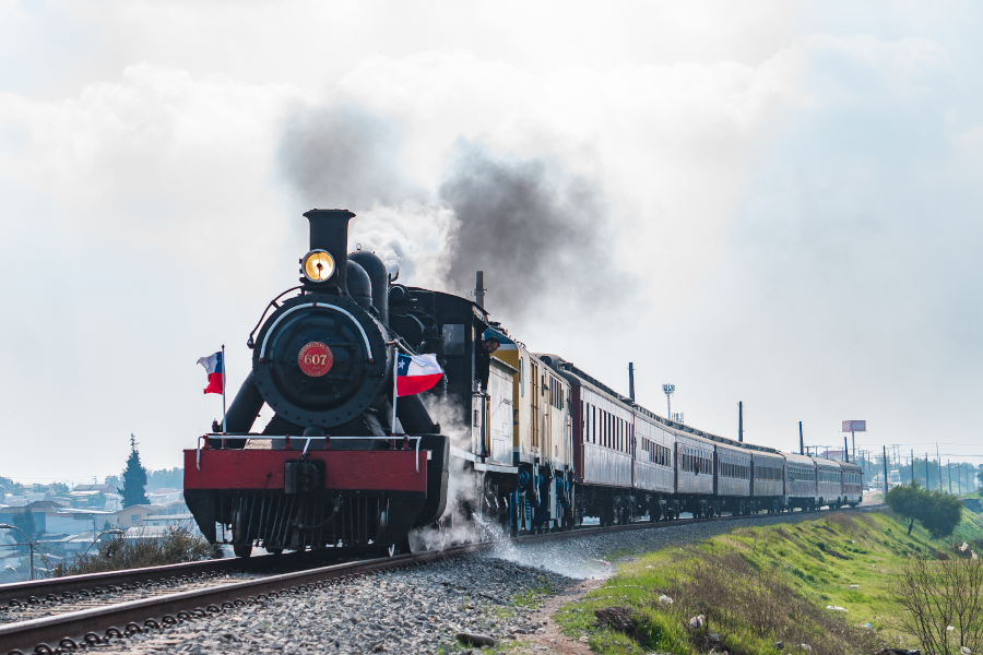 Antigua locomotora a vapor con banderas chilenas avanzando por la vía.
