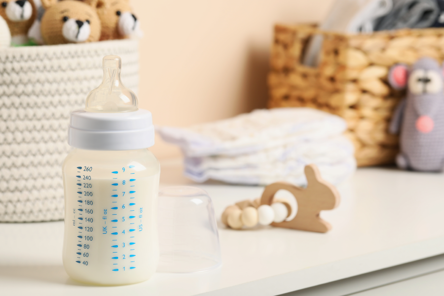 Mamadera con leche en primer plano, rodeada de pañales y juguetes.