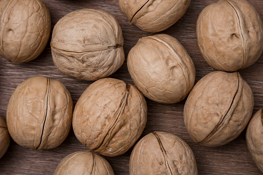 Whole, unpeeled walnuts in their brown shells on wooden surface. 