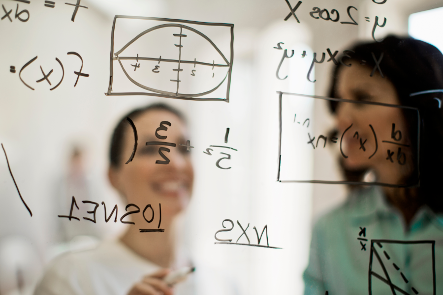 Mathematical equations written on glass with two women in background.