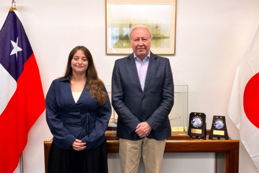 En la imagen aparece la estudiante Daniela Gallardo junto al Embajador de Chile en Japón, Ricardo Rojas. Detras de ellos hay un arrimo, un cuadro y a un costado de la estudiante, la bandera chilena.