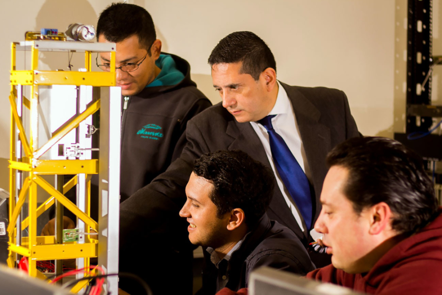 La foto muestra a cuatro hombres interactuando en un laboratorio