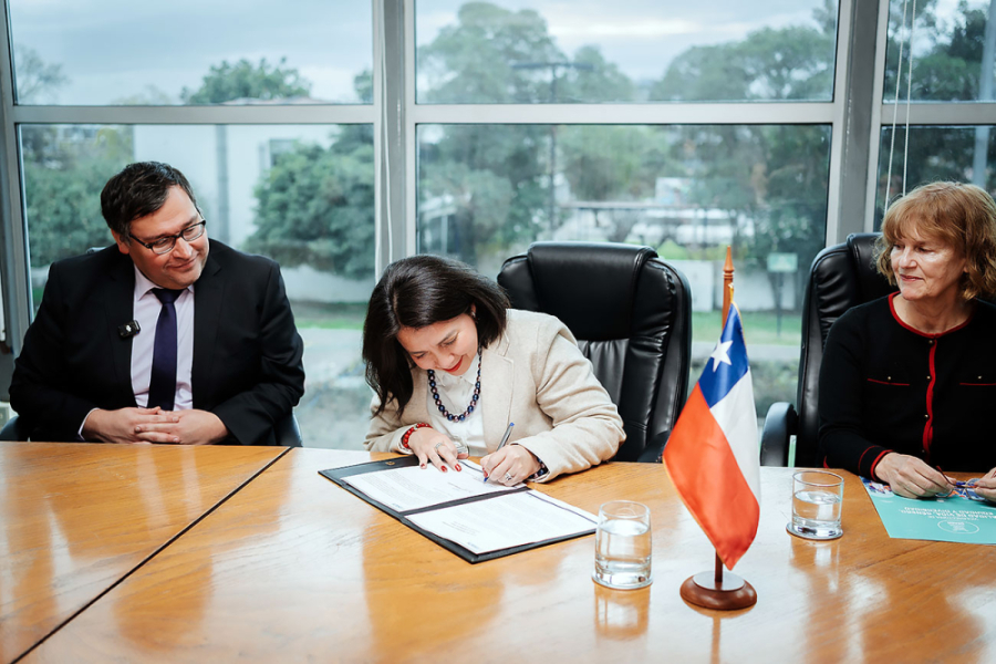 La imagen muestra a la vicerrectora firmando el documento en la sala de reuniones de rectoría. A su lado están otras autoridades que participaron de la firma