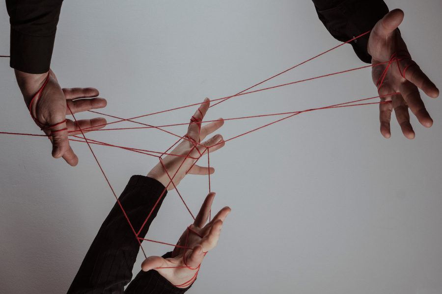 Manos entrelazadas y controladas por hilos rojos como si fueran marionetas.