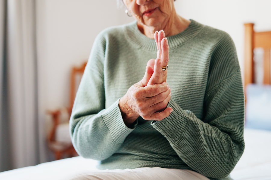 Una mujer de edad avanzada sentada masajeándose suavemente la mano temblorosa.