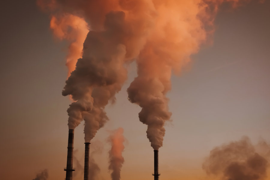 Industrial smokestacks releasing thick plumes of smoke at sunset.