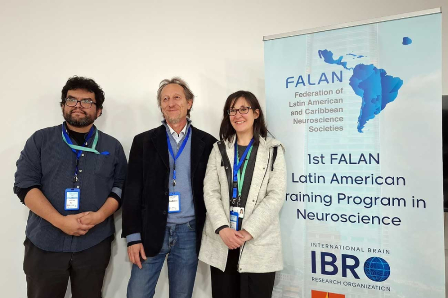 La imagen muestra a tres participantes de la actividad, dos hombres y una mujer, posando junto al pendón del evento