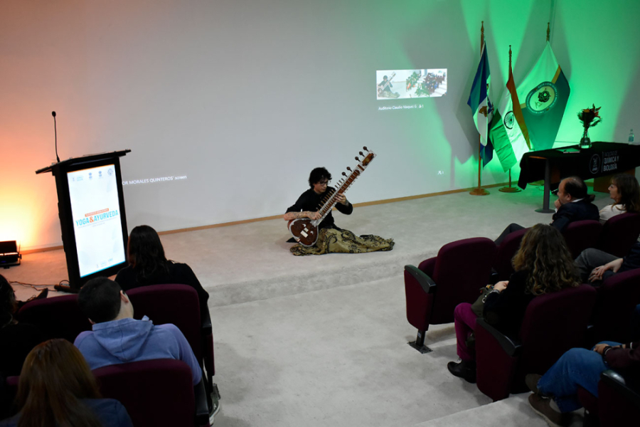 En la imagen aparece un músico tocando la cítara frente a parte de la comunidad estudiantil que llenó el Auditorio de la Facultad de Química y Biología