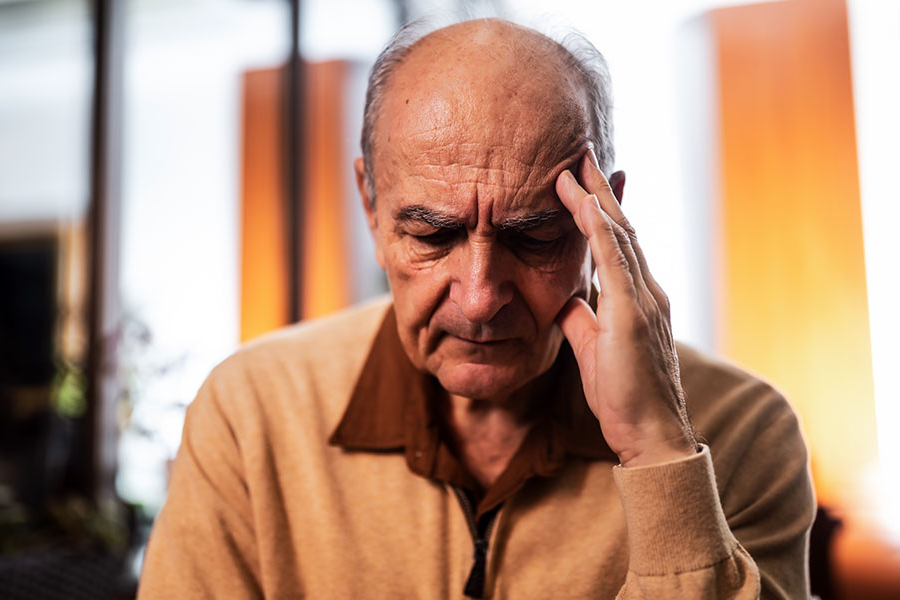 Un hombre de edad avanzada se lleva la mano a la frente, con aspecto ansioso y cansado.